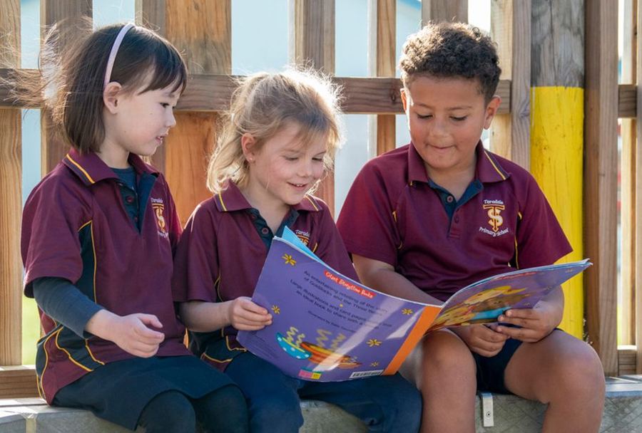 Three students sharing a picture book outdoors